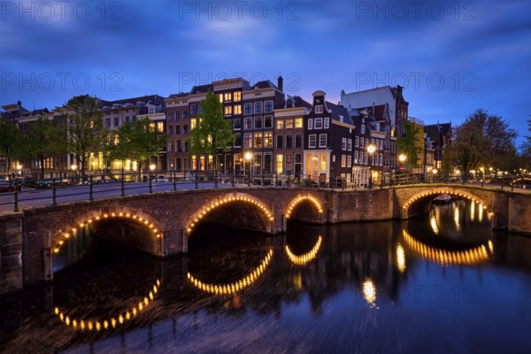 Night view of Amsterdam cityscape with canal, bridge and medieval houses in the evening twilight illuminated. Amsterdam, Netherlands