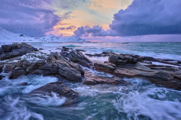 Waves of Norwegian sea on rocky coast in fjord on sunset with sun. Skagsanden beach, Lofoten islands, Norway, Europe