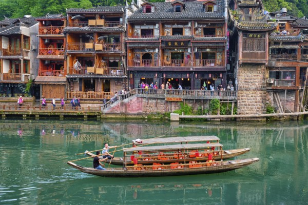 FENGHUANG, CHINA, APRIL 21, 2018: Chinese tourist attraction destination, Feng Huang Ancient Town (Phoenix Ancient Town) on Tuo Jiang River with bridge and tourist boat. Hunan Province, China, Asia