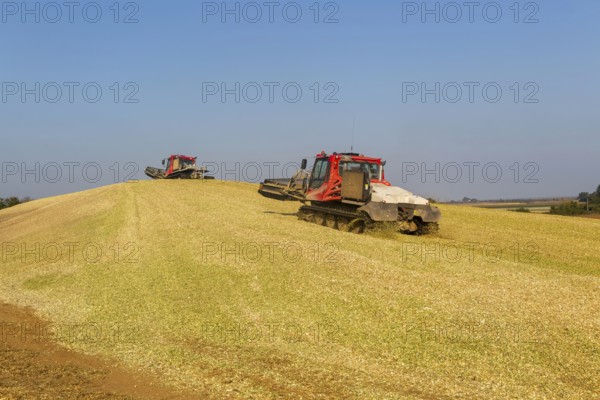 Piston Bully tracked bulldozer vehicles building silage clamp of sweetcorn maize in field stored for biofuel, Alderton, Suffolk, England, UK