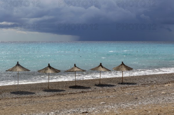 Line of sunshades along the beach with dark storm clouds offshore, Dhermi, Albania, Europe