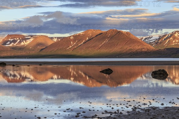 Fjord, low tide, stones, mountains reflected in the water, evening light, cloudy mood, Thingeyri, Westfjords, Iceland, Europe