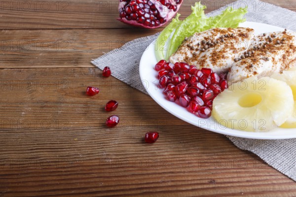 Fried chicken fillets with lettuce, pineapple and pomegranate seeds on brown wooden background, copy space, close up