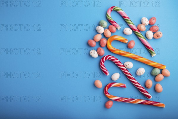 Colorful multicolored candies on a blue background. Christmas cane, chocolate eggs, caramel dragees. copy space, top view, flat lay