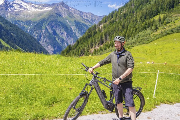 Man in sportswear standing next to his bicycle on a green meadow, surrounded by mountains and blue sky, Klein Tibet, Zillertal, Austria, Europe