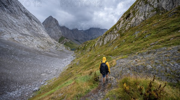 A mountaineer on a hiking trail with lush green vegetation, hiking trail to the Wolayerseehütte, cloudy mountain peaks, Carnic Alps, Carnic High Trail, Carinthia, Austria, Europe