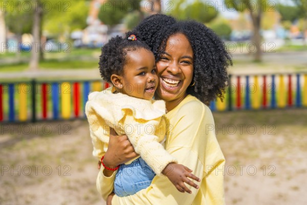 Happy african american mother embracing and holding in arms her little daughter on a park
