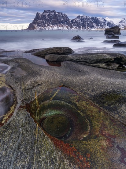 Rocks on the beach, rock formation Eye of Utakleiv, or Dragon's Eye, snow-capped mountains behind, Utakleiv, Vestvågøya, Lofoten, Norway, Europe