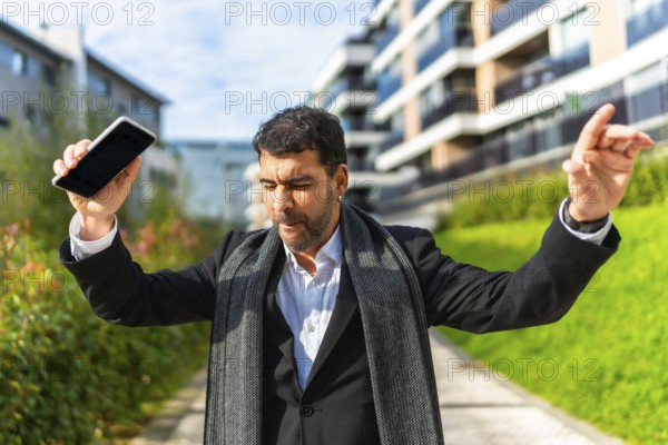 Happy businessman dancing celebrating while holding mobile phone outdoors int he city in a sunny day of autumn
