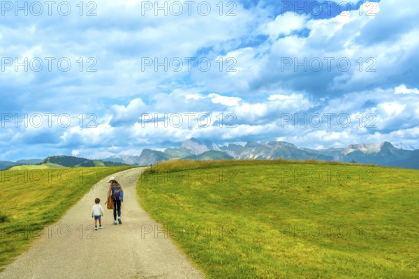 Mother and child walking on a path at alpe di siusi enjoying the landscape in the dolomites on a sunny summer day