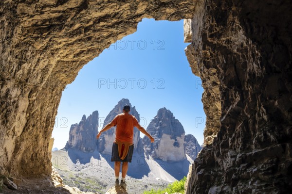 Hiker enjoying the breathtaking view of the tre cime di lavaredo from inside a Tre Cime Cave in the italian dolomites