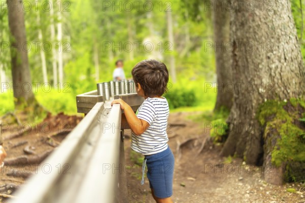 Curious kid having fun with water game in the forest of lake braies, famous destination in dolomites