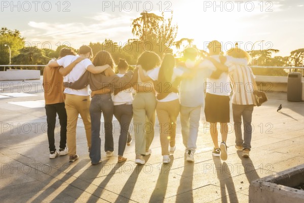 Rear view of friends embracing walking together along the city during sunset