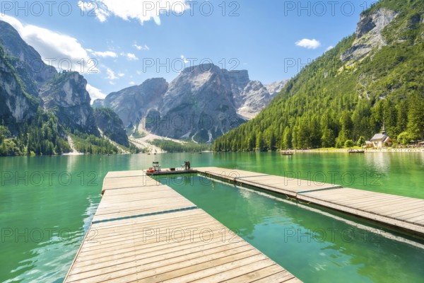 Wooden pier reflecting in the emerald waters of lake braies, surrounded by the dolomites on a sunny summer day in south tyrol
