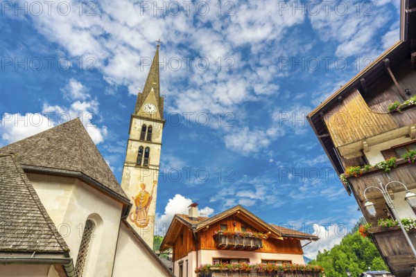 Picturesque view of alleghe village in the italian dolomites, featuring a church tower, traditional houses with flower filled balconies, and a vibrant blue sky