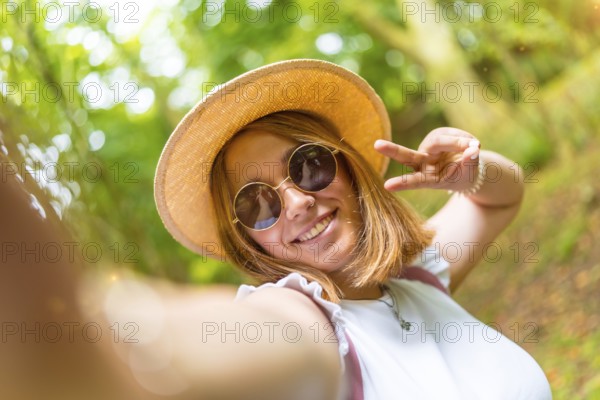 Personal point of view of a beauty young caucasian woman gesturing success with fingers while taking a selfie hiking in the forest