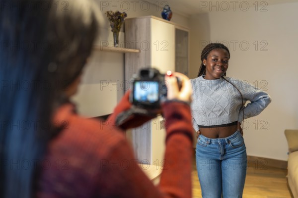 Photographer capturing her beautiful friend posing joyfully in the cozy living room, celebrating friendship and creativity in a relaxed atmosphere