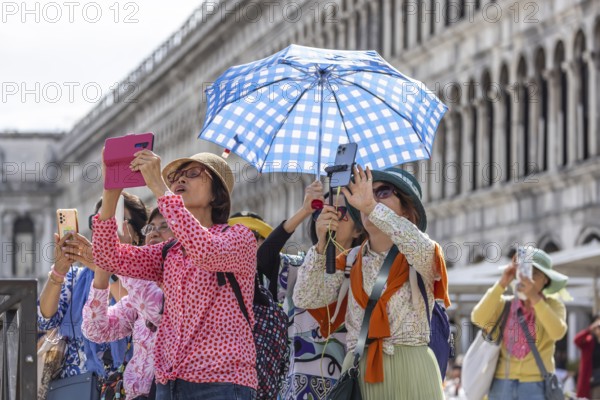Tourists from Asia with mobile phones and parasols taking photos. Souvenir photo of St Mark's Square, Venice, Venice, Italy, Europe