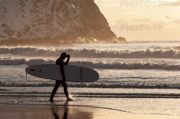 Surfer with surfboard under his arm on the beach of Unnstad, winter surfing, Lofoten Island Vestvågøya Lofoten, Northern Norway, Norway, Europe