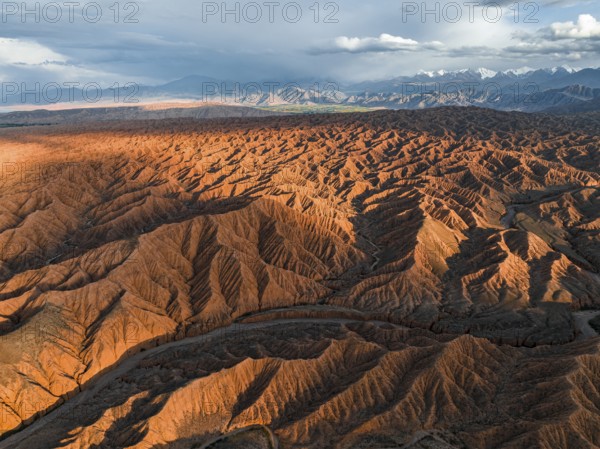 River bed runs through a landscape of eroded hills, badlands at sunset, mountain peaks of the Tian Shan Mountains in the background, aerial view, Canyon of the Forgotten Rivers, Issyk Kul, Kyrgyzstan, Asia