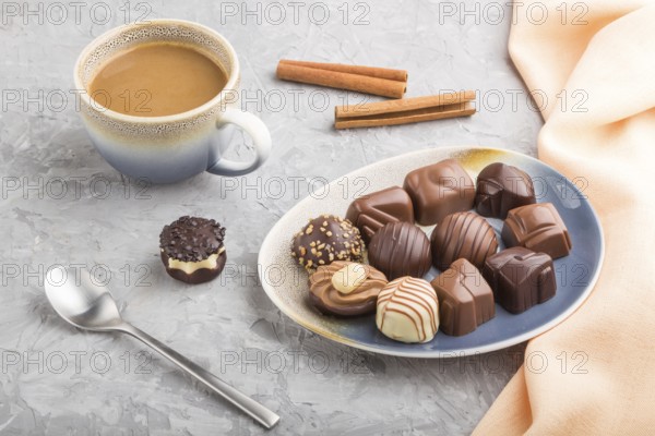 Different chocolate candies and a cup of coffee on a gray concrete background and orange textile. side view, close up