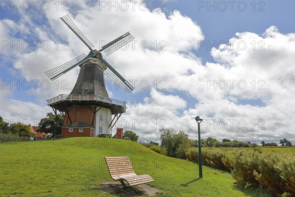 A windmill in front of a dramatic blue sky, surrounded by green meadows with a deckchair, Greetsiel, East Frisia, Lower Saxony, Germany, Europe