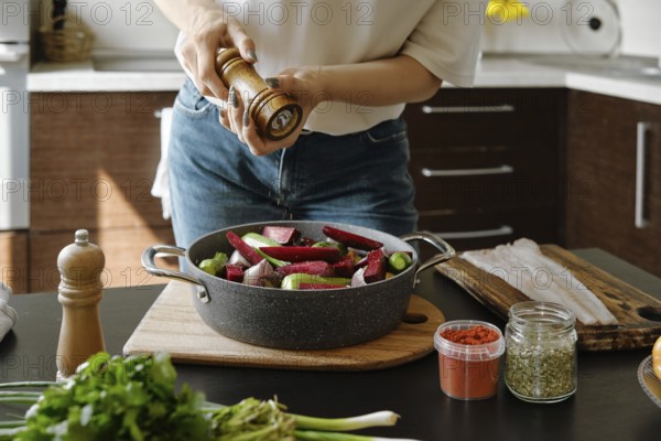 Close-up view of female hands sprinkle pepper from manual spice mill on vegetables in a baking pan
