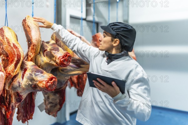 Woman butcher using digital tablet working inside a cold storage room in a meat processing factory
