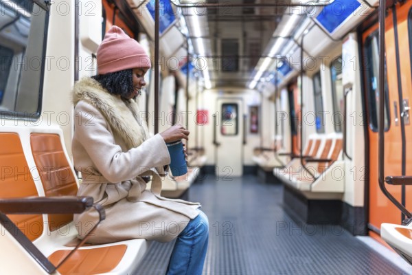 Passenger opening a reusable coffee cup while enjoying a quiet moment on a nearly empty subway train during the winter commute