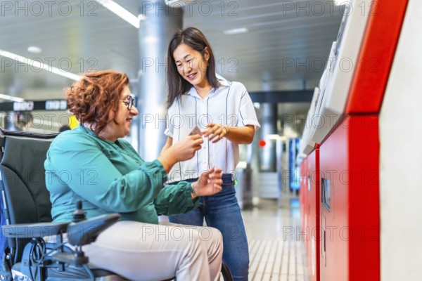 Chinese smiling caregiver buying metro ticket to a caucasian adult disabled woman in wheelchair