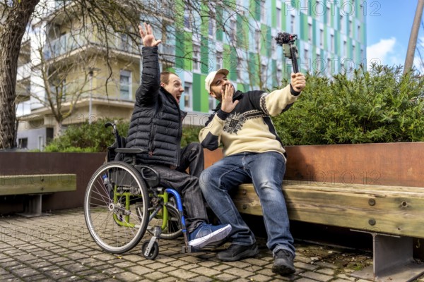 Two cheerful content creators, one in a wheelchair, are recording a video blog in an urban setting, using a gimbal for stabilized footage