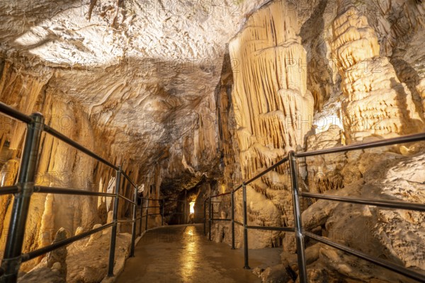 Tourists walking on illuminated pathway, admiring stalactites and stalagmites inside postojna cave, a famous natural attraction in slovenia