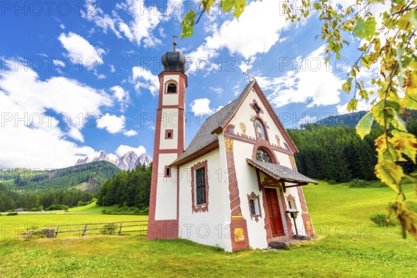 Charming st. Magdalena church nestled in a green meadow, with the majestic odle mountains and lush forests creating a stunning backdrop