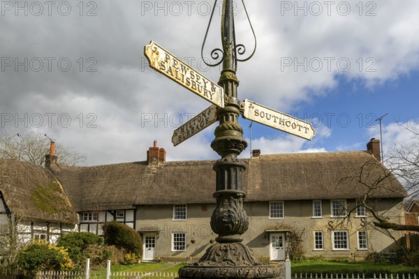 Historic signpost with direction painters, thatched cottages in village of Pewsey, Wiltshire, England, UK