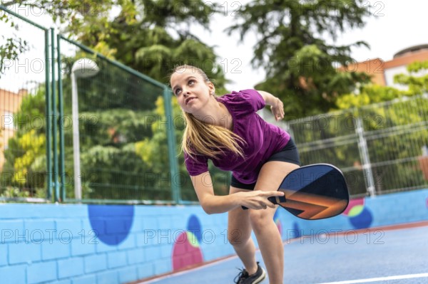 Energetic and sportive blonde young woman playing pickelball in an outdoor court