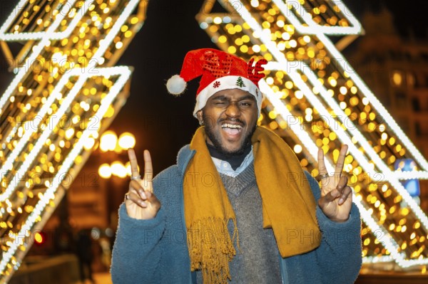 Portrait of a fun cool african young casual man gesturing success wearing a Santa hat at night in the city in Christmas