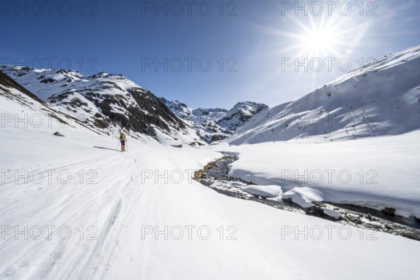 Ski tourer in the snow by a mountain stream in the Funtauna Valley, Sonnenstern, Graubünden Haute Route, Albula Alps, Rhaetian Alps, Graubünden, Switzerland, Europe