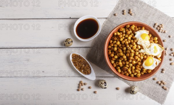 Fried chickpeas with quail eggs and spices in a clay plate on white wooden background, top view, copy space
