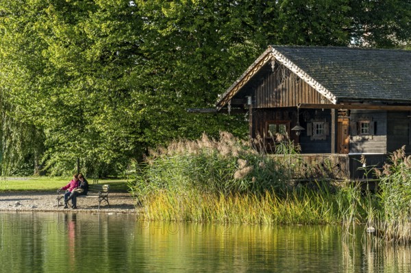 Wooden hut with common reed (Phragmites australis), two woman on a park bench, shore of Lake Schliersee, spa garden Markt Schliersee, Upper Bavaria, Bavaria, Germany, Europe
