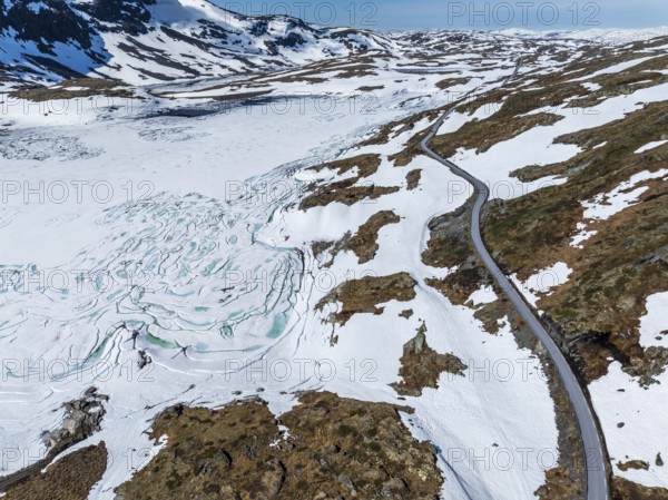 Aerial view of mountain crossing Sognefjellsvegen, along frozen lake Prestesteinsvatnet, Sognefjell, Norway, Europe