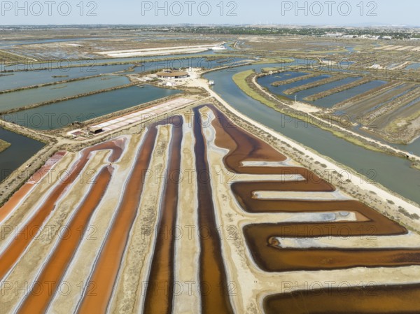 Saline ponds at the salt works near Chiclana de la Frontera. The orange-red colour depends on the level of salinity and is directly caused by the algae Dunaliella salina and brine shrimp. Aerial view. Drone shot. Bahía de Cádiz Nature Reserve, Cádiz province, Andalusia, Spain, Europe