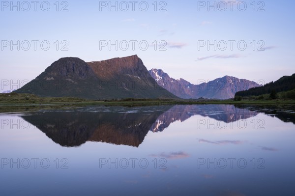 Landscape on the Lofoten Islands. Vagspollen bay, with Offersoykammen mountain behind it. The mountain Stornappstinden on Flakstadoya in the background. The mountains are reflected in the water. At night at the time of the midnight sun in good weather. Early summer. Vestvagoya, Lofoten, Norway, Europe