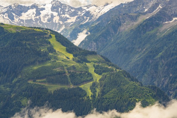 Alpine mountain landscape with green forests and alpine pastures in front of snow-covered mountain peaks and clouds, Zillertal, Austria, Germany, Europe