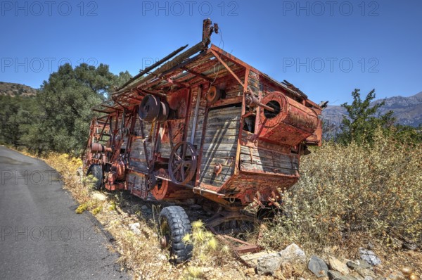 Dilapidated, rusted combine harvester next to the road under blue sky, wrecked vehicle, Crete, Greek Islands, Greece, Europe