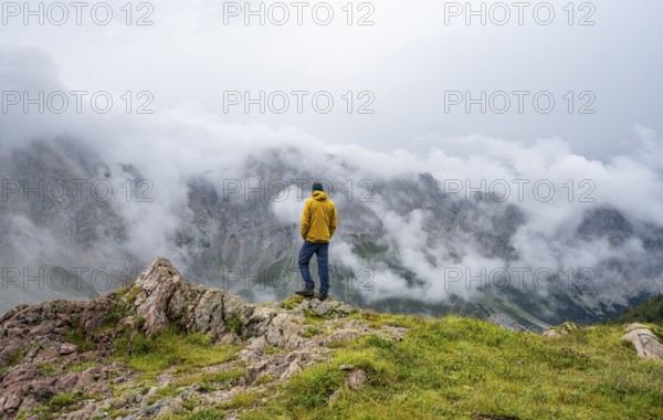 Mountaineer with yellow jacket looking at mountain landscape, cloudy rocky mountain peaks Wolayer Köpf and Biegenköpfe, Carnic Alps, Carnic High Trail, Carinthia, Austria, Europe