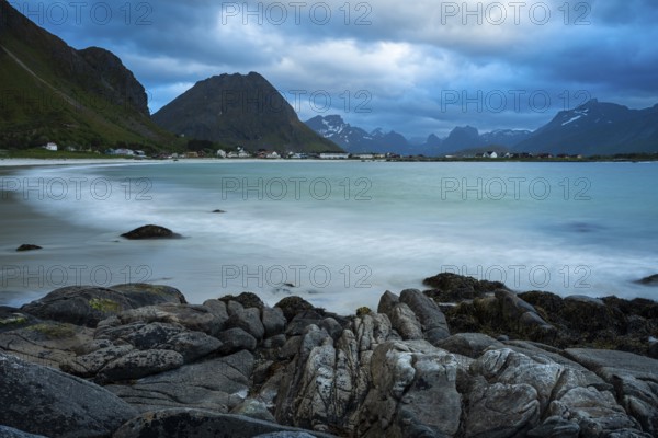 Landscape on the Lofoten Islands. The village of Ramberg, with rocks and sea and the sandy beach (Rambergstranda) in front. Mountains in the background. At night at the time of the midnight sun. Clouds in the sky. Early summer. Long exposure. Ramberg, Flakstadoya, Lofoten, Norway, Europe