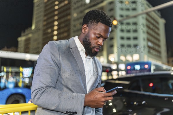 Young businessman using smartphone on city street at night, with blurred buildings and traffic in background