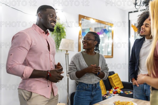 Multi-ethnic friends standing around a table with snacks talking relaxed during party at home