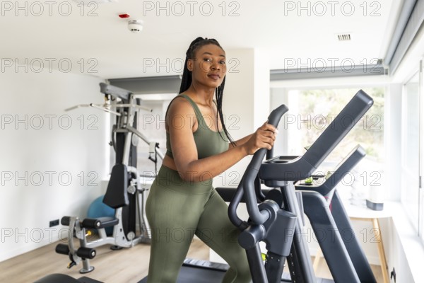 Businesswoman wearing olive green activewear using elliptical cross trainer in hotel fitness center during business trip
