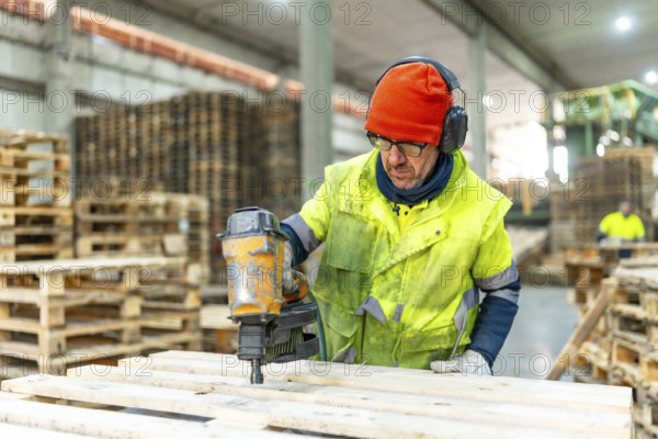Man manual worker using compressed air gun to arrange pallets to reuse in a recycling plant warehouse